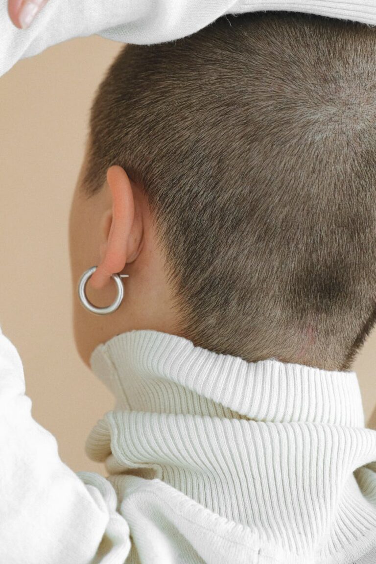 Back view of a woman in a turtleneck, showcasing a buzz cut and hoop earring.